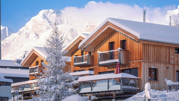 A wooden chalet with balconies, surrounded by snow-covered mountains.