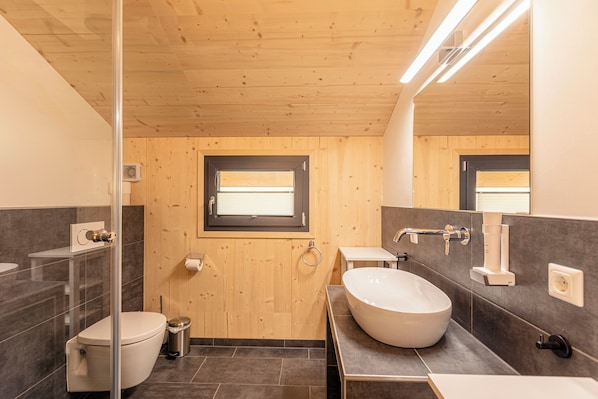 A modern bathroom with a wooden ceiling, a large window, a white sink, and a toilet. - Bergeralm Chalets by ALPS RESORTS (Steinach am Brenner)