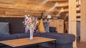 A wooden interior with a sofa, a table with a vase of dried flowers, and a wooden cabinet in the background.