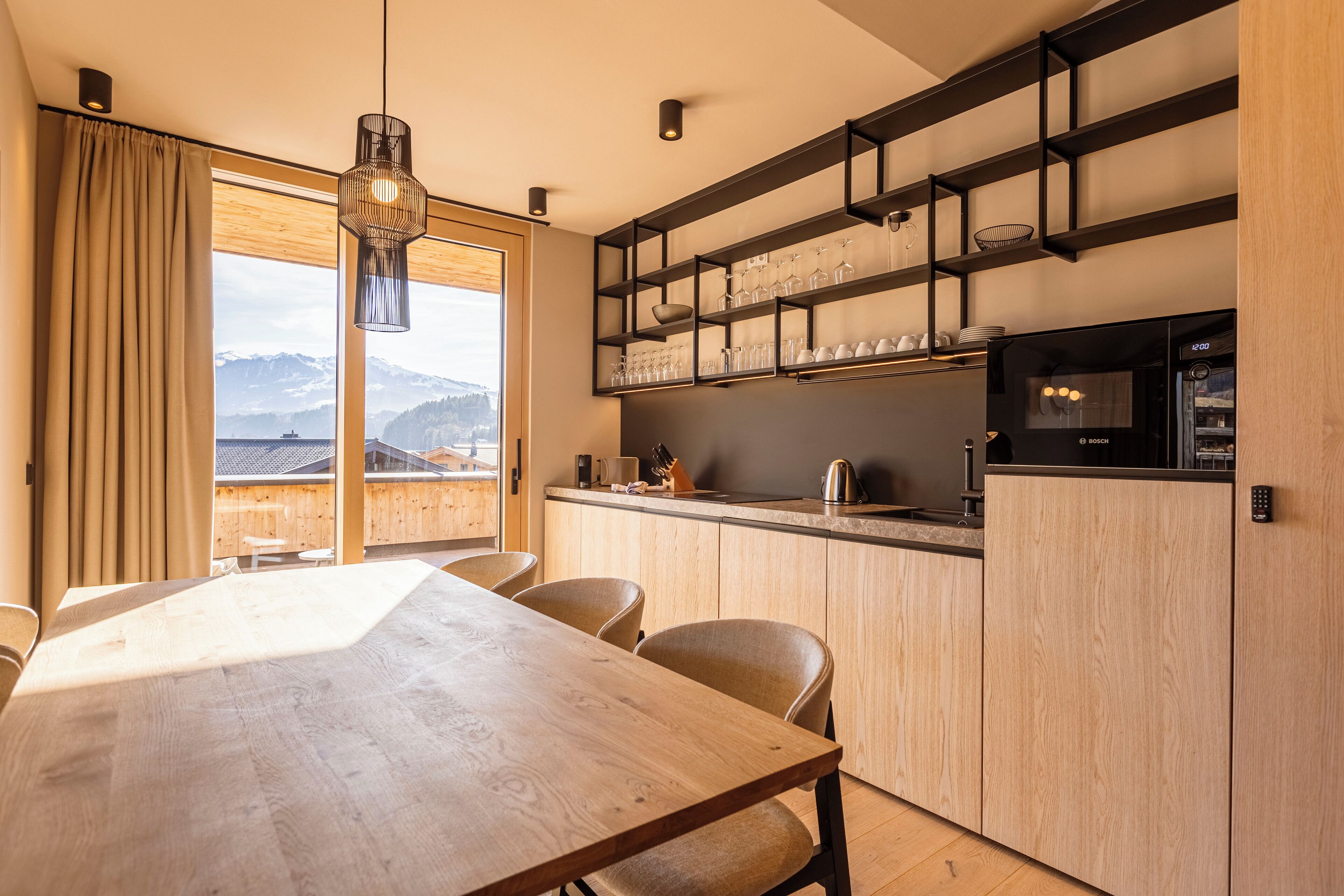 A modern kitchen with a wooden table and chairs, a built-in wine rack, and a view of mountains through large windows.