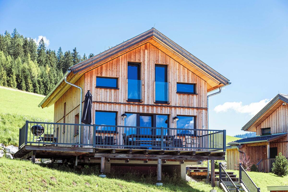 Un chalé de madera con balcón, ventanas amplias y vistas del paisaje circundante.