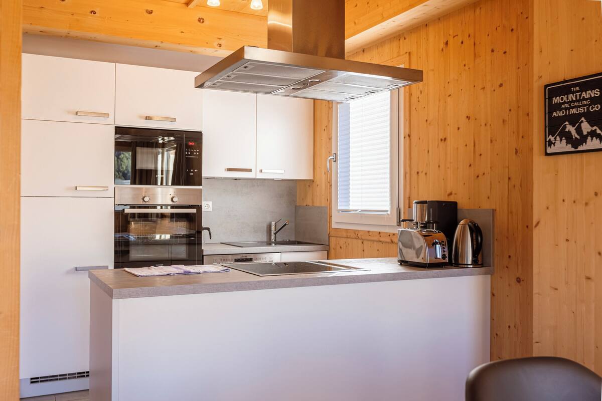 Cocina moderna con armarios blancos, electrodomésticos de acero inoxidable e interior de madera.