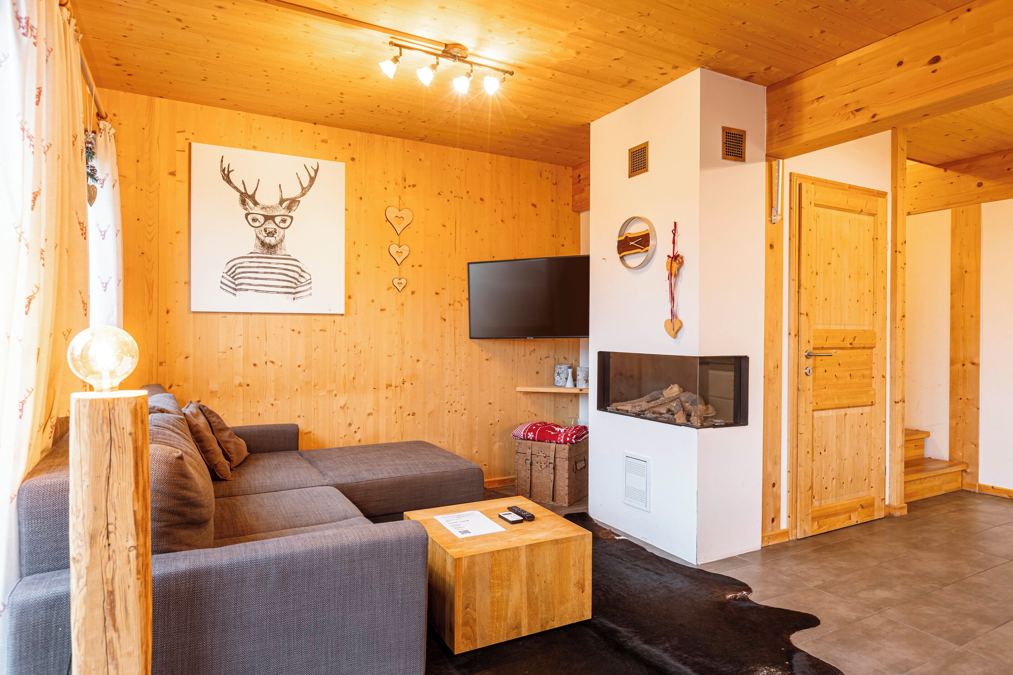 A cozy living room with a wooden ceiling, a gray sofa, a wooden coffee table, a flat-screen TV, and a fireplace.