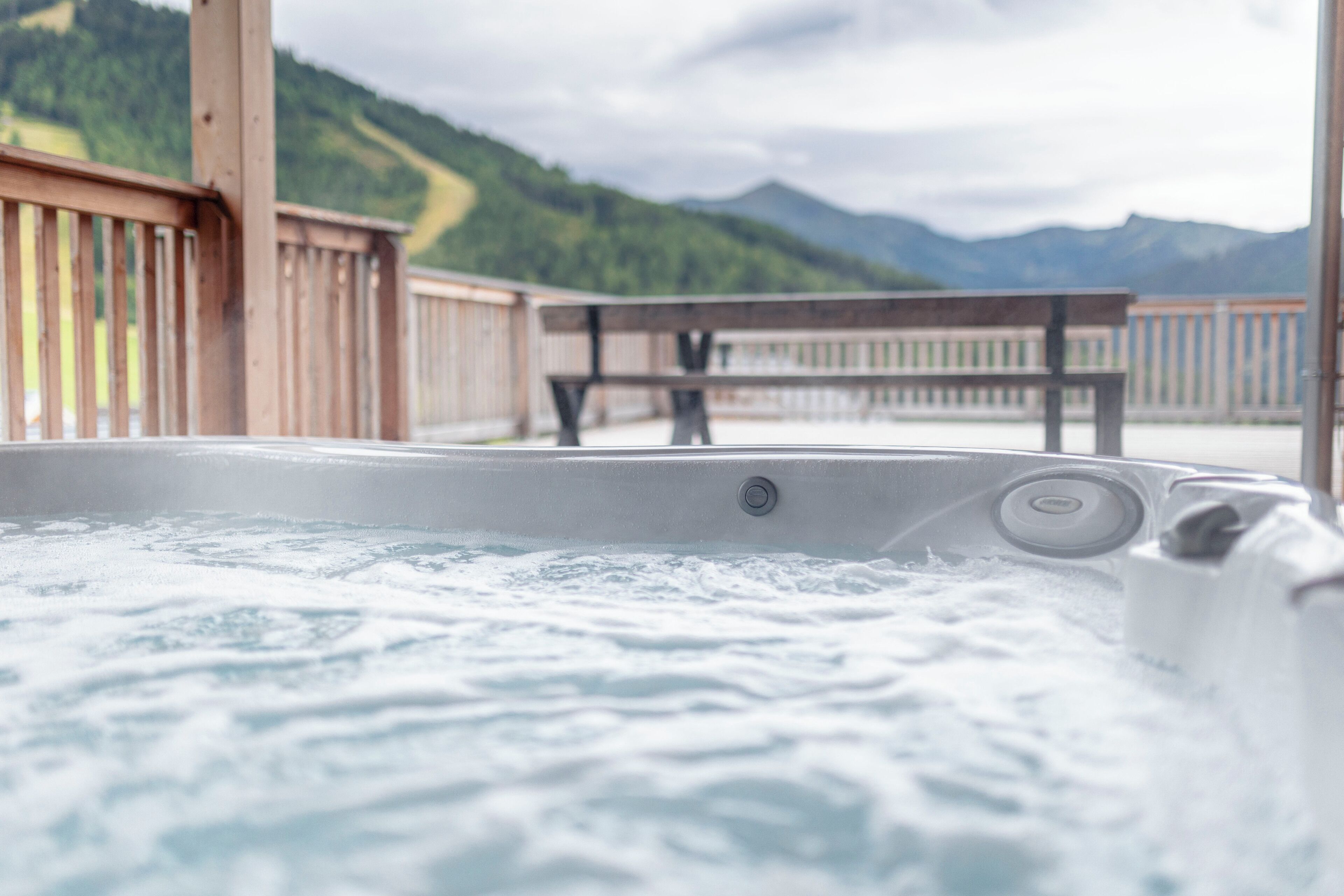 Un jacuzzi con muelle de madera y bancos, con vistas a un paisaje montañoso.