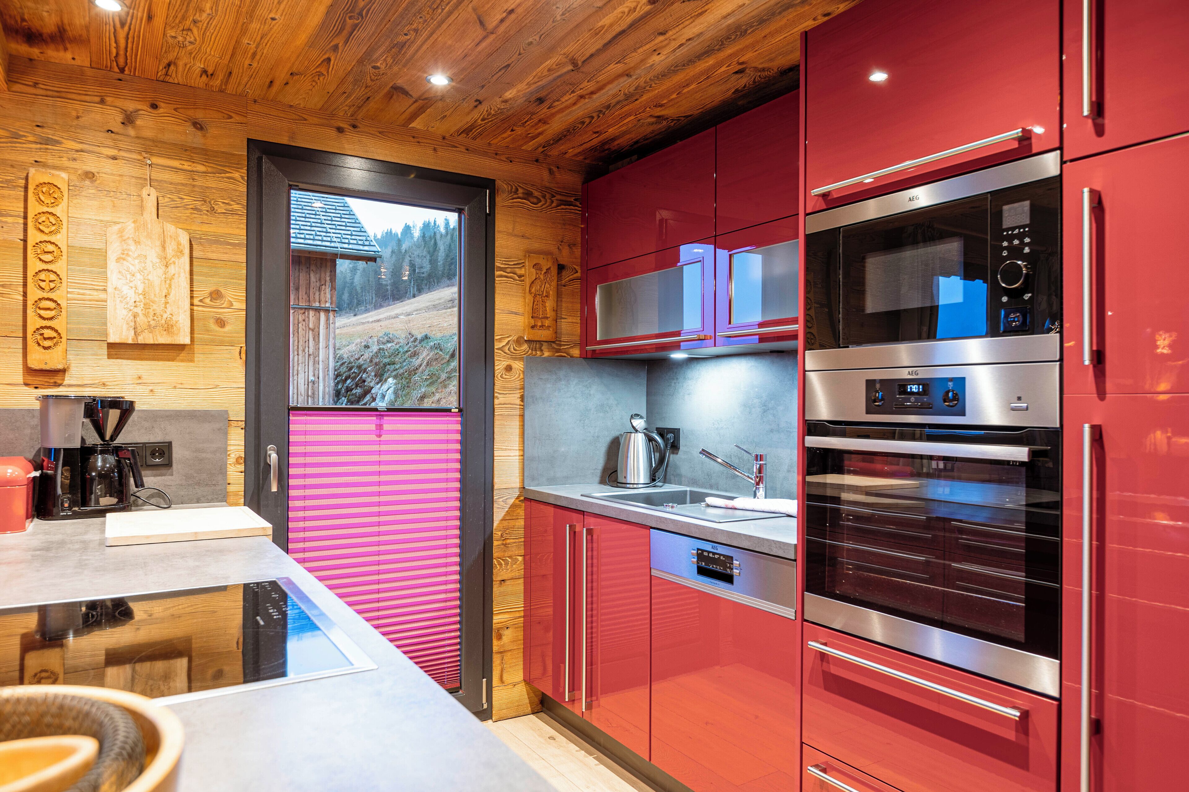 Una cocina moderna con armarios rojos, electrodomésticos de acero inoxidable y techo de madera.