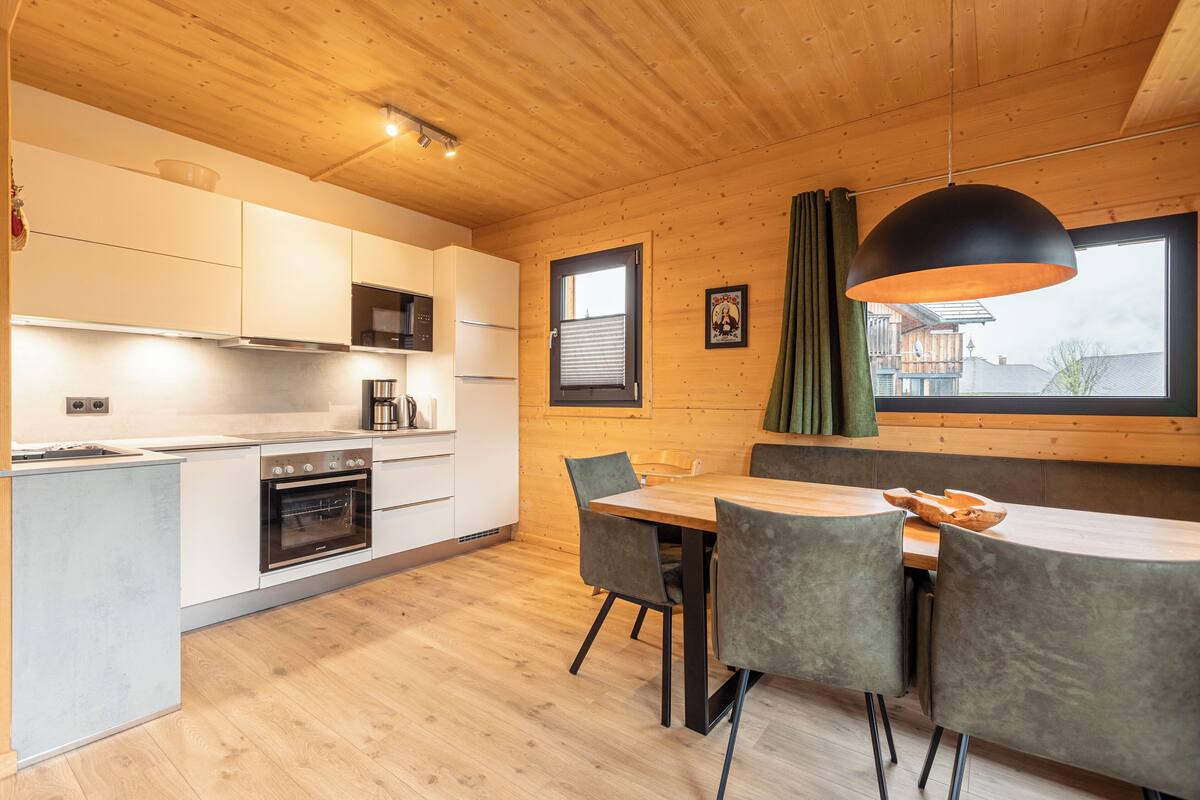 Una cocina moderna con armarios blancos, techo de madera y un comedor con mesa y sillas.