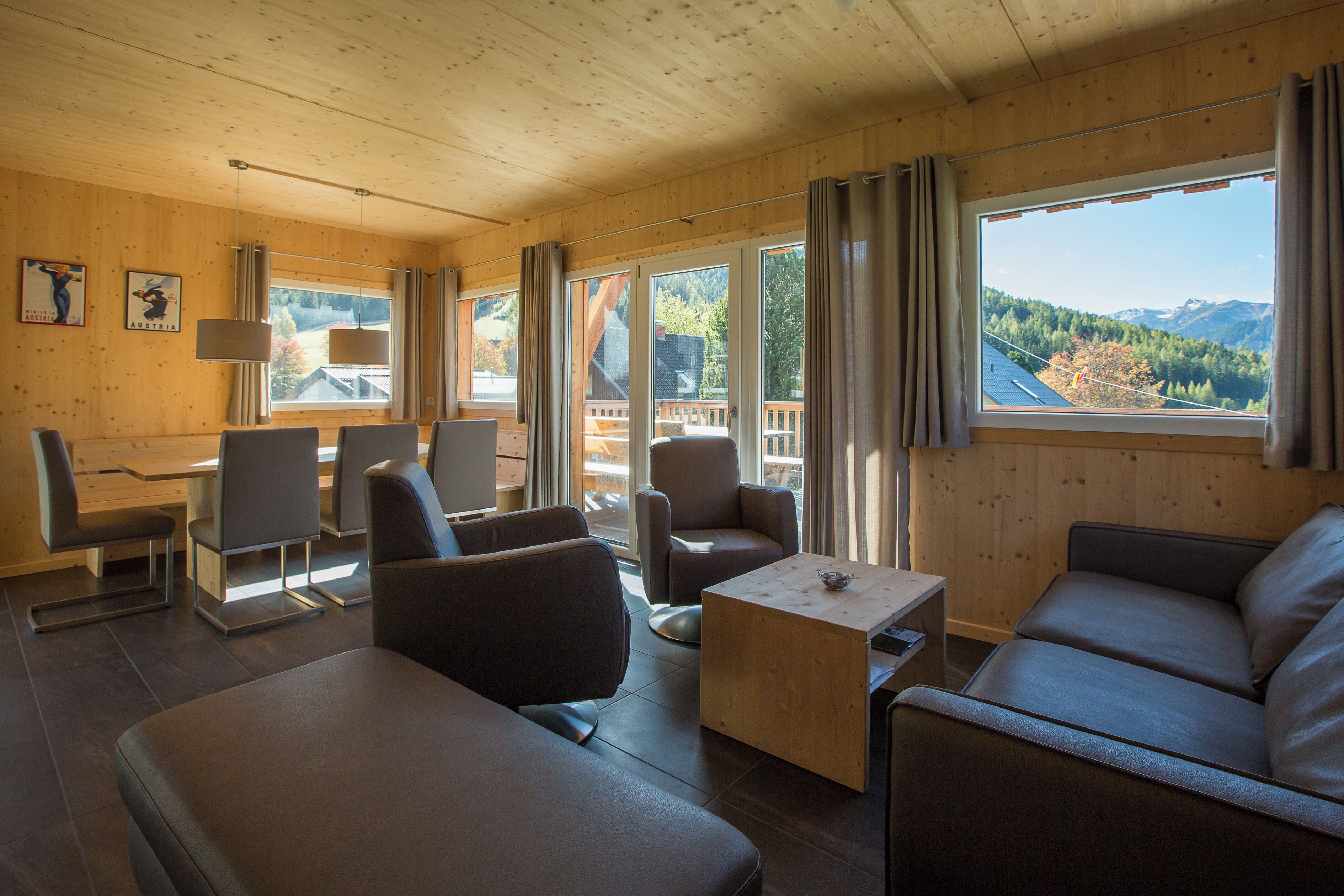L’intérieur d’un chalet en bois comprend un canapé, des fauteuils, une table et de grandes fenêtres donnant sur une vue imprenable sur les montagnes.