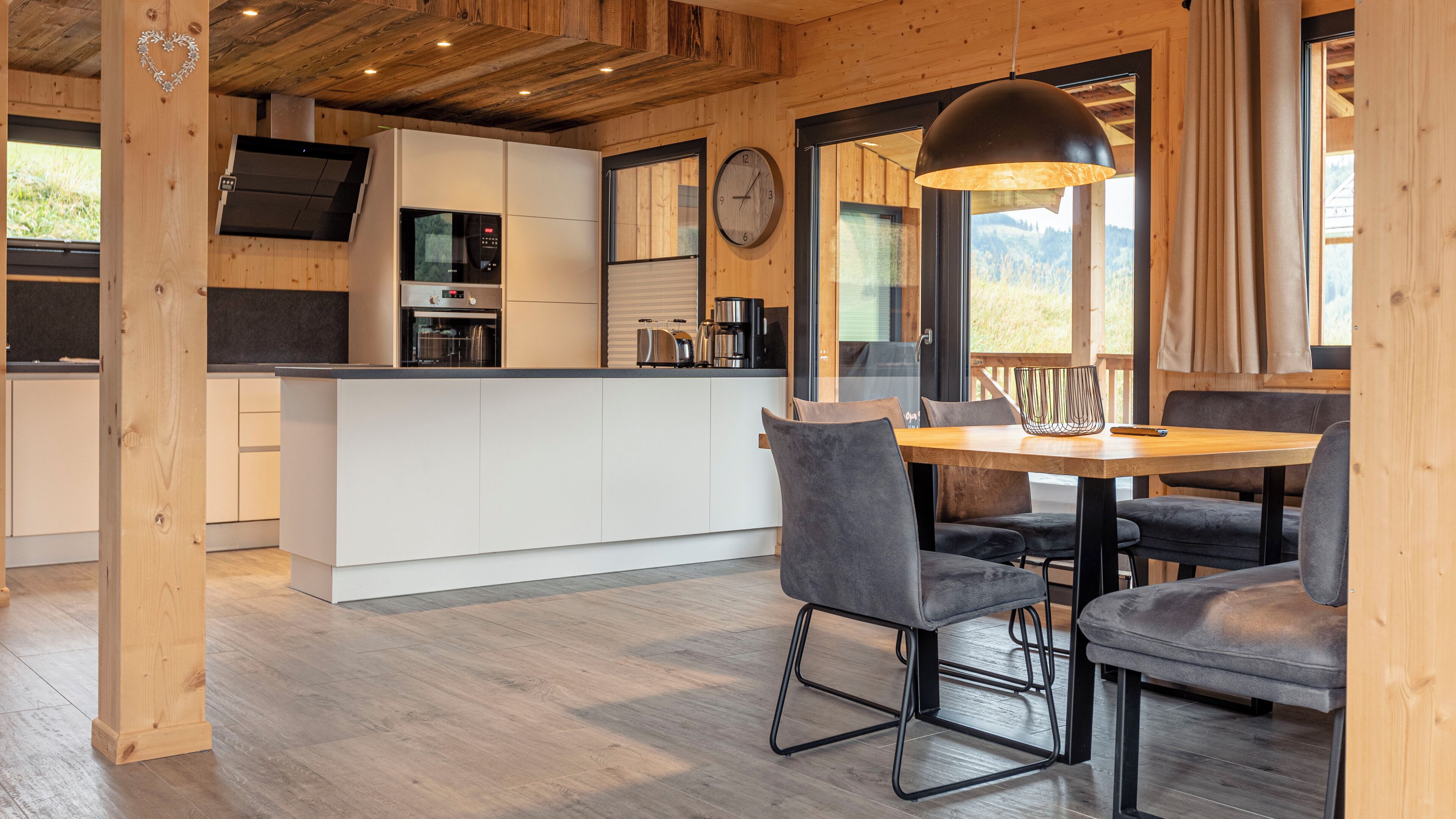 A modern kitchen with white cabinets, a central island, and a dining area with grey chairs and a wooden table.