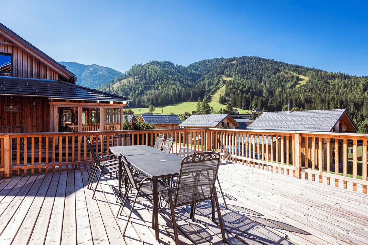 Una terraza de madera con mesa y sillas, con vistas a un paisaje montañoso.