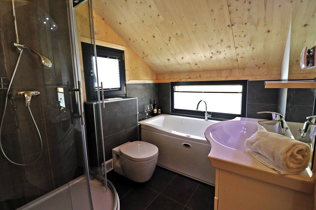 Un baño moderno con ducha envuelta en cristal, bañera y tocador con lavamanos y toalla.