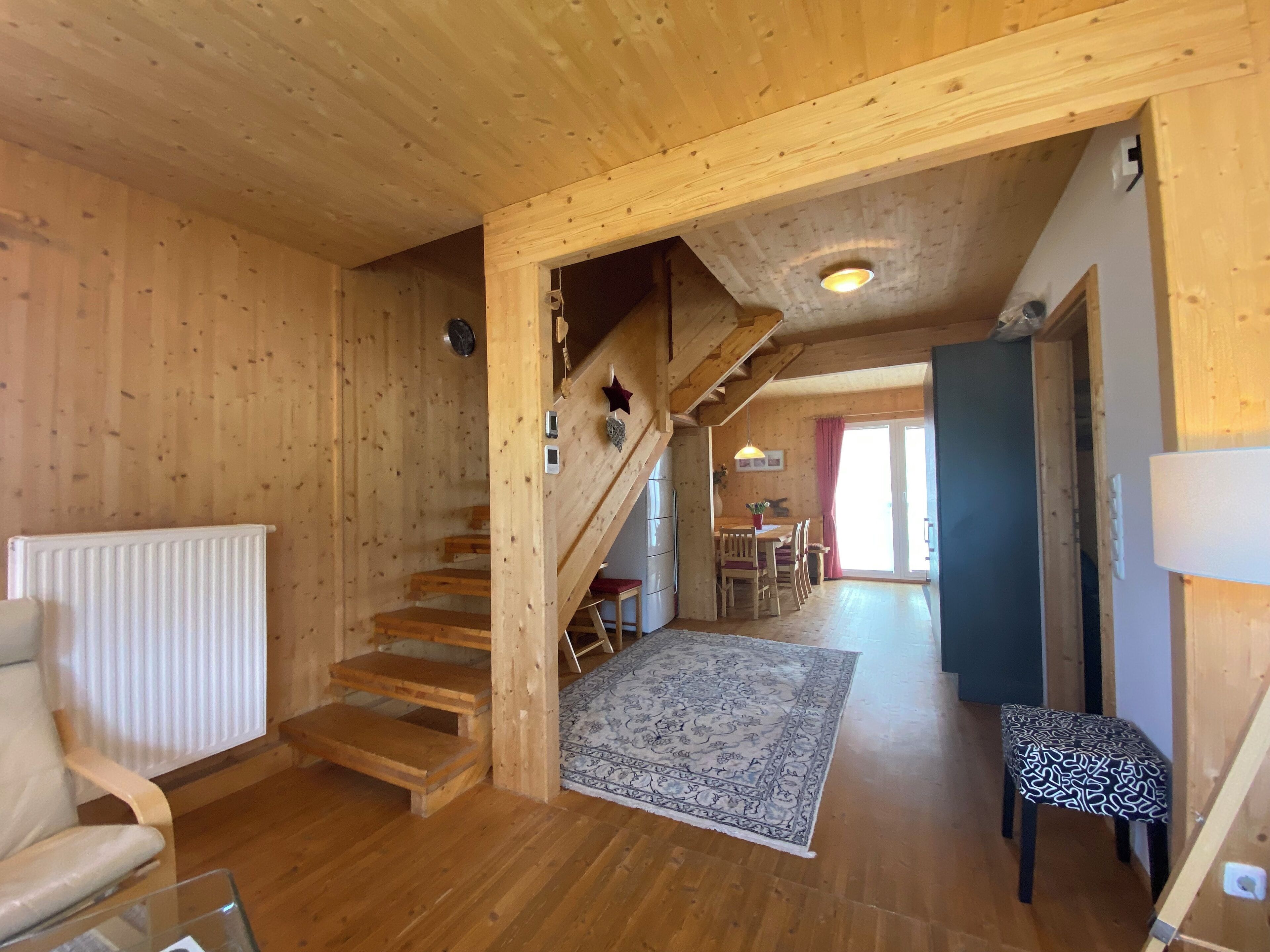 A wooden interior with a staircase, a dining area, and a view to the outside.