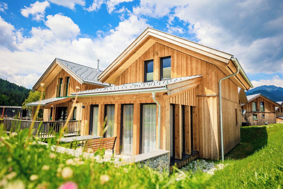 Una cabaña de madera con techo inclinado, ventanas amplias y base de piedra.