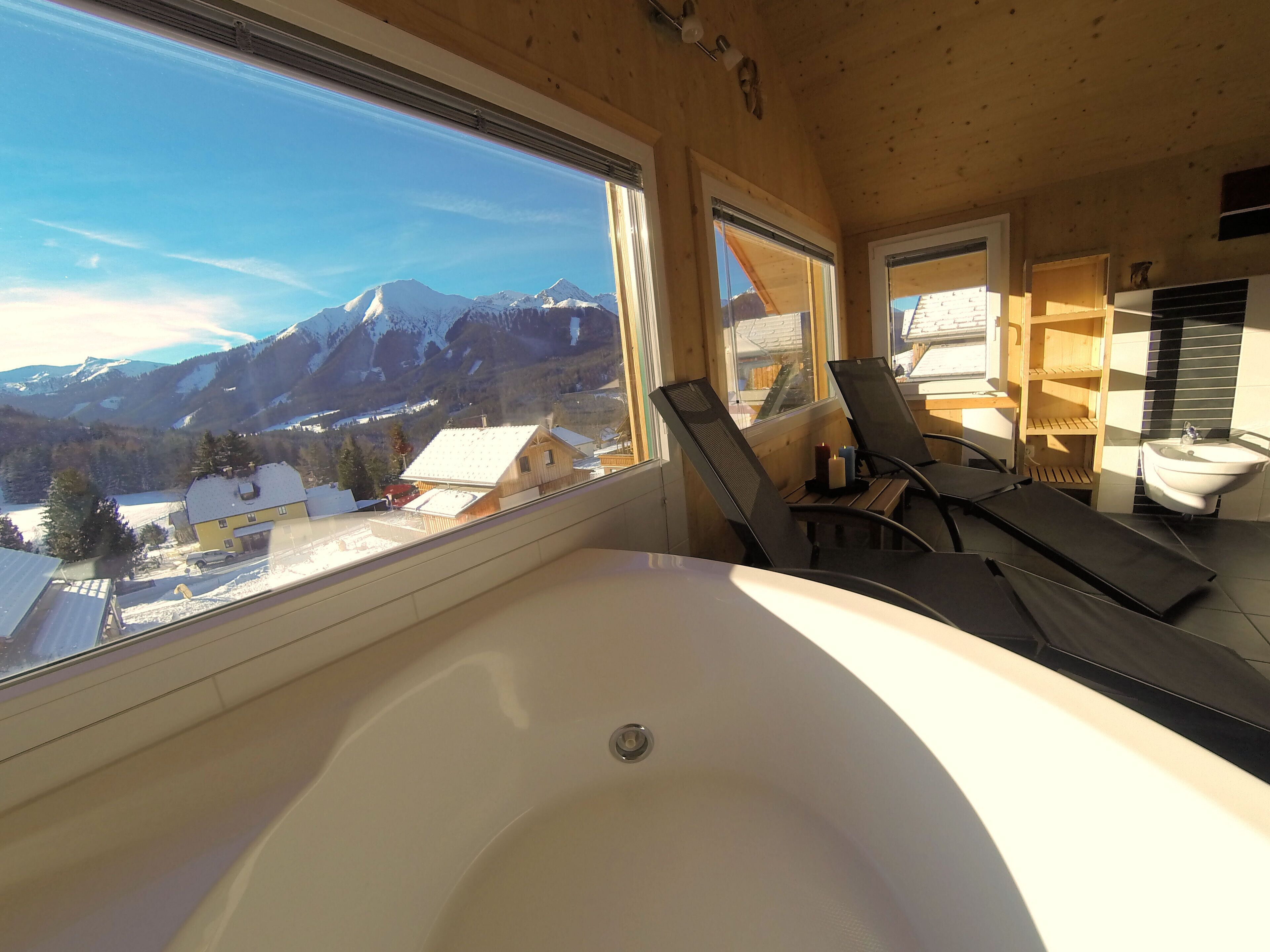 A room with a large bathtub, wooden walls, and a view of snow-covered mountains.
