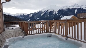 A wooden deck with a hot tub, surrounded by snow-covered mountains and a wooden cabin. - Almdorf Hohentauern by ALPS RESORTS (Hohentauern)