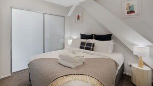 A bedroom with a bed, a bedside table, a lamp, and a large window.