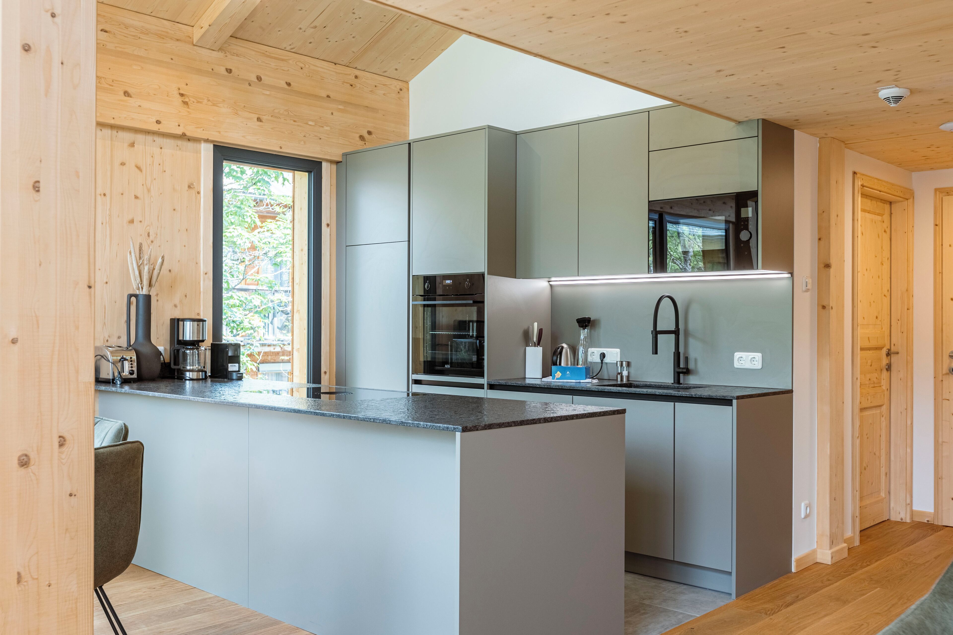 A modern kitchen with grey cabinets, a built-in oven, and a large island with a sink.