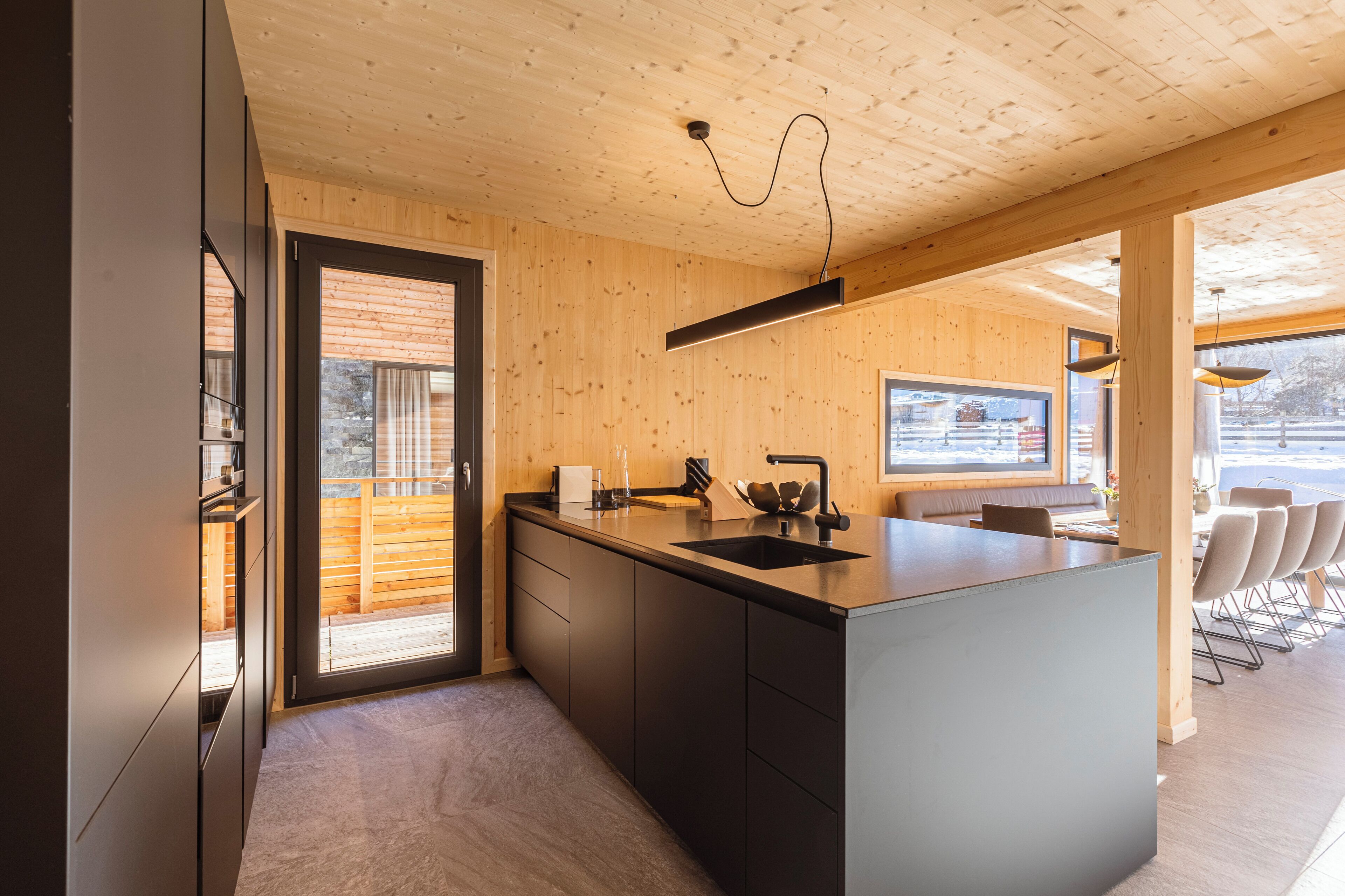 A modern kitchen with wooden walls, a large island, and a view of the outdoors.