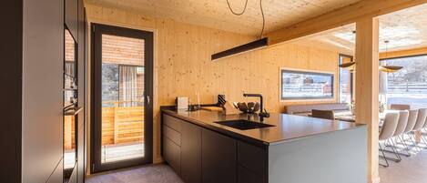 A modern kitchen with wooden walls, a large island, and a view of the outdoors.