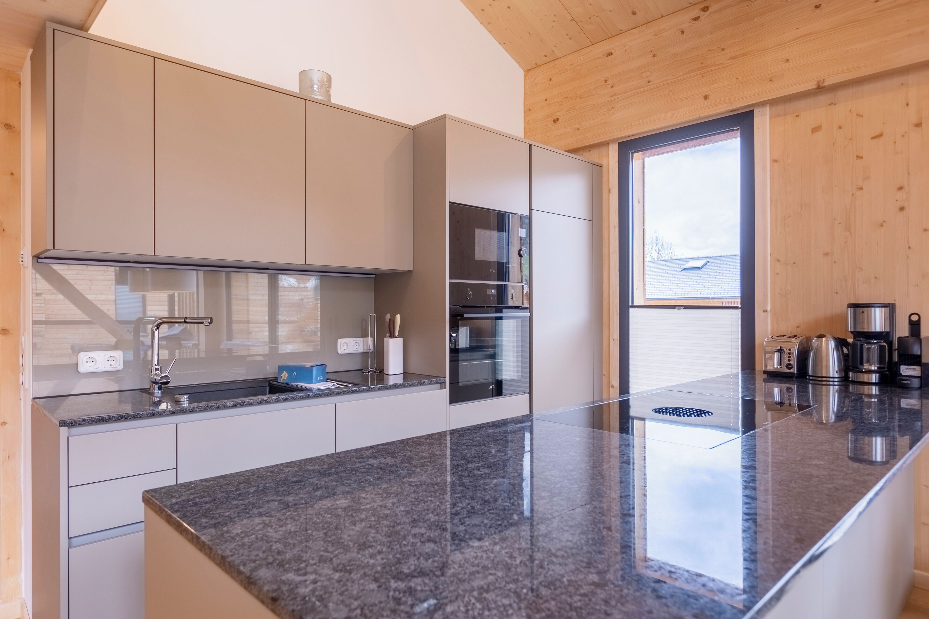A modern kitchen with a granite countertop, stainless steel appliances, and wooden ceiling.