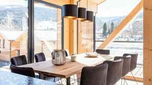 A wooden interior with a large dining table, black chairs, and a modern pendant light.