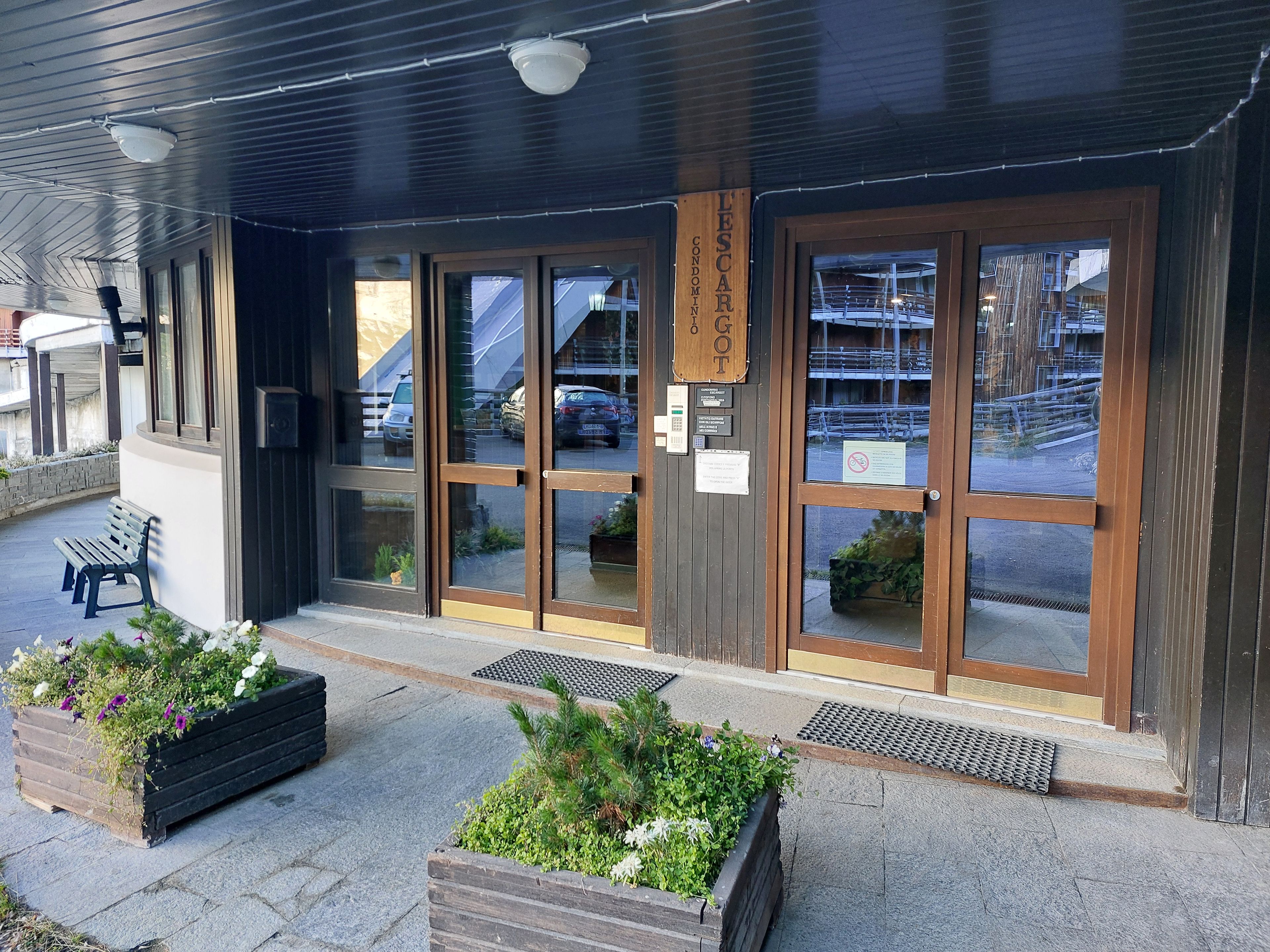 A building entrance with a wooden sign, glass doors, and a bench outside.