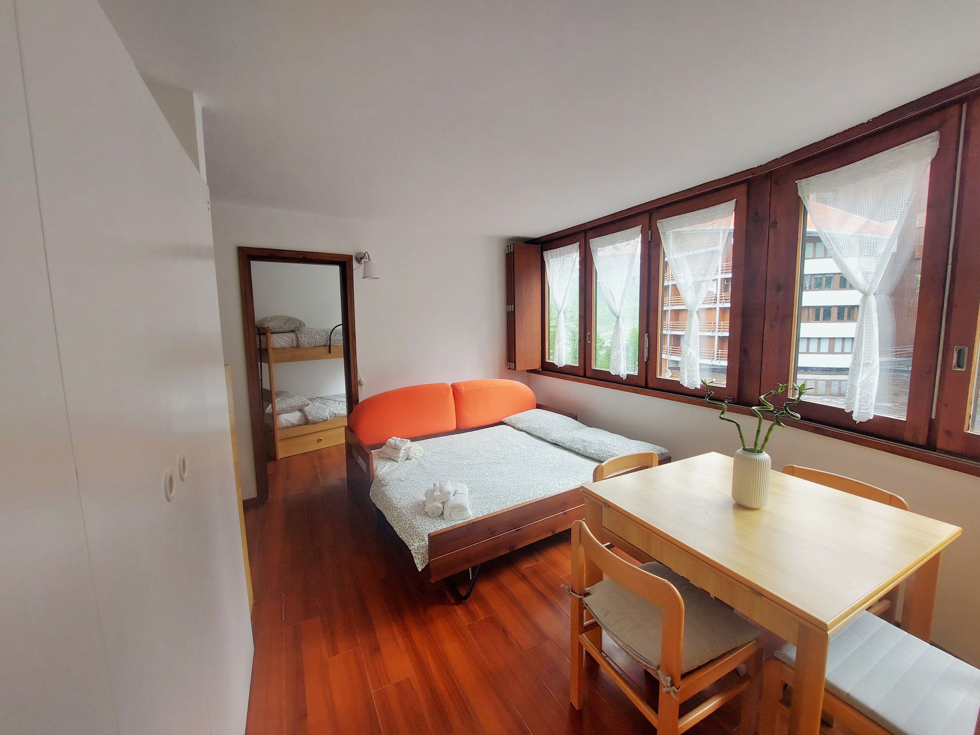 A compact room with a bunk bed, a small desk, and a window with curtains.