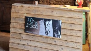 Un interior rústico con pared de piedra, escalera de madera y mostrador de madera con un letrero con motivos ecuestres.