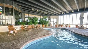 An indoor swimming pool with tiled edges, surrounded by wooden chairs and potted plants. - Sands Beach Club #112 (Myrtle Beach)