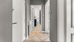 A narrow hallway with white doors, a wooden floor, and a view into a bathroom with a toilet and sink.