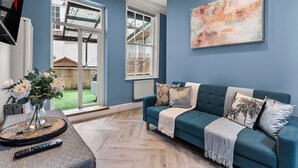 A living room with a teal sofa, a large abstract painting, and a view of a garden through a glass door.