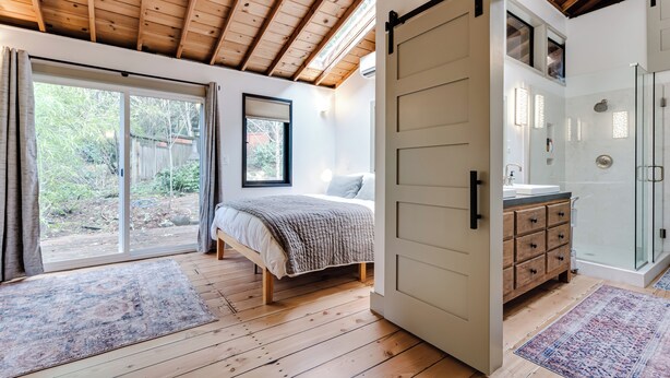 Un dormitorio con una cama grande, una puerta corredera hacia el baño y vistas al exterior.