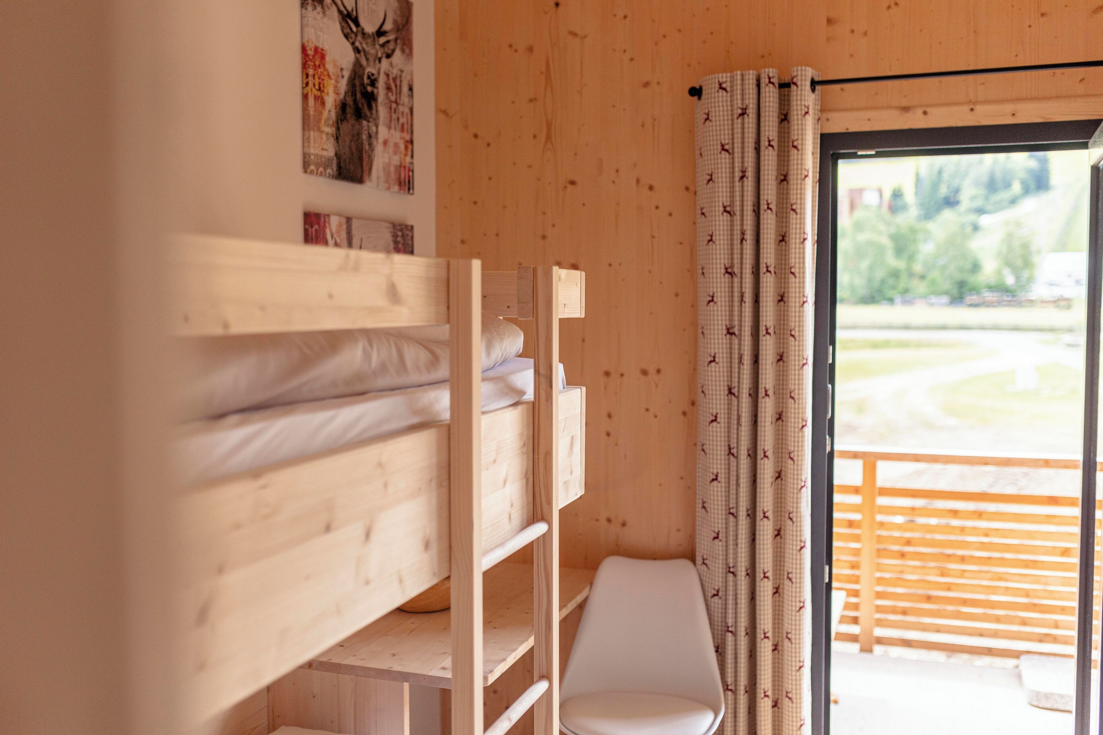 A wooden bunk bed with a white chair and a window with curtains.
