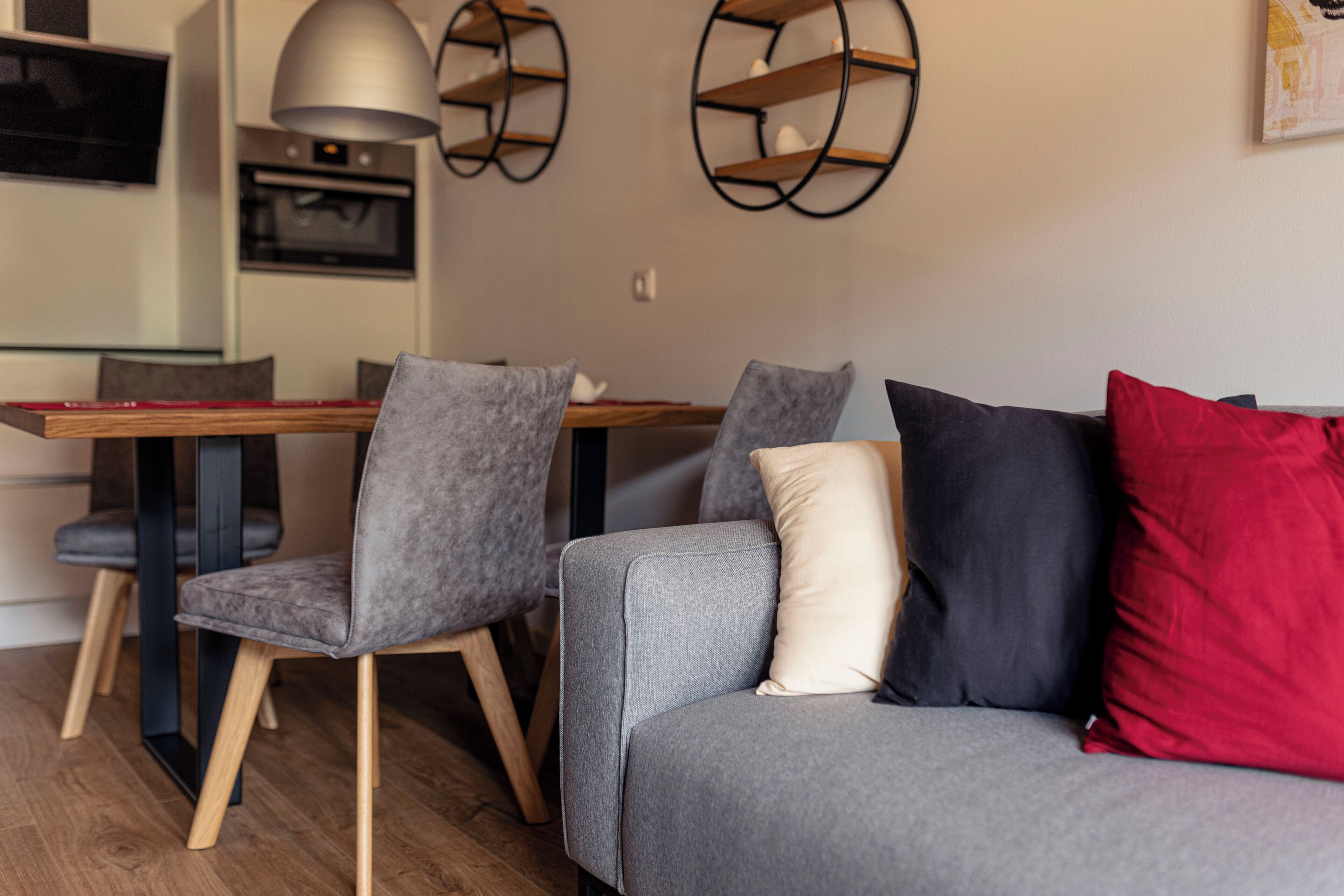 Una sala moderna con un sofá gris, dos sillones grises y una mesa de comedor de madera.