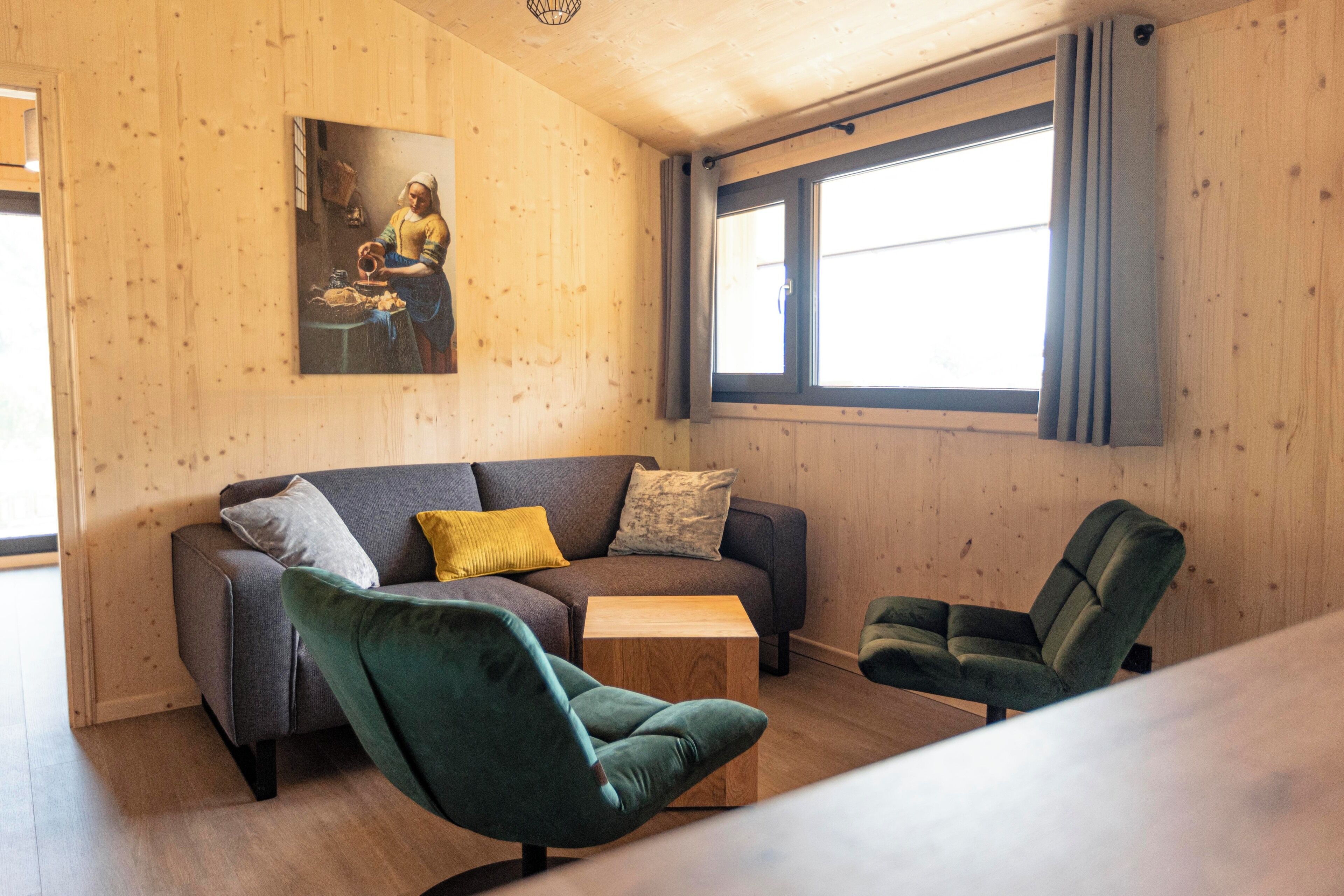 Una stanza accogliente con un divano grigio, due poltrone verdi, un tavolino in legno e un quadro appeso al muro.