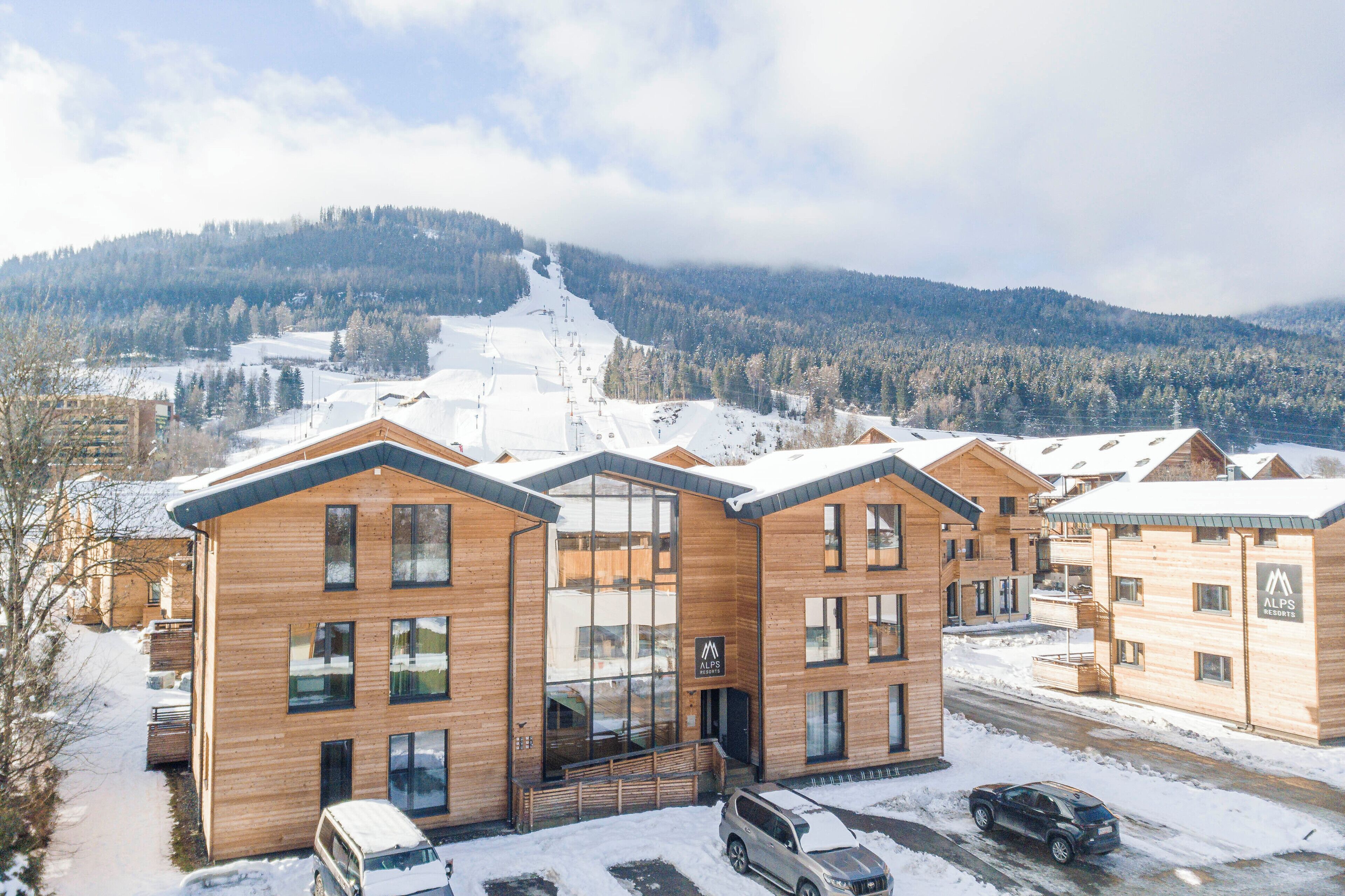 Un bâtiment moderne en bois, doté de grandes fenêtres, avec un télésiège visible en arrière-plan.