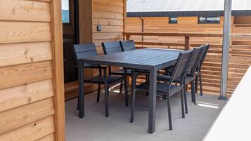 Una terraza de madera con una mesa y sillas, un muro de madera y una barandilla de metal.