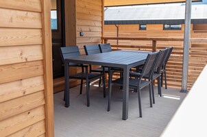 Una terraza de madera con una mesa y sillas, un muro de madera y una barandilla de metal.