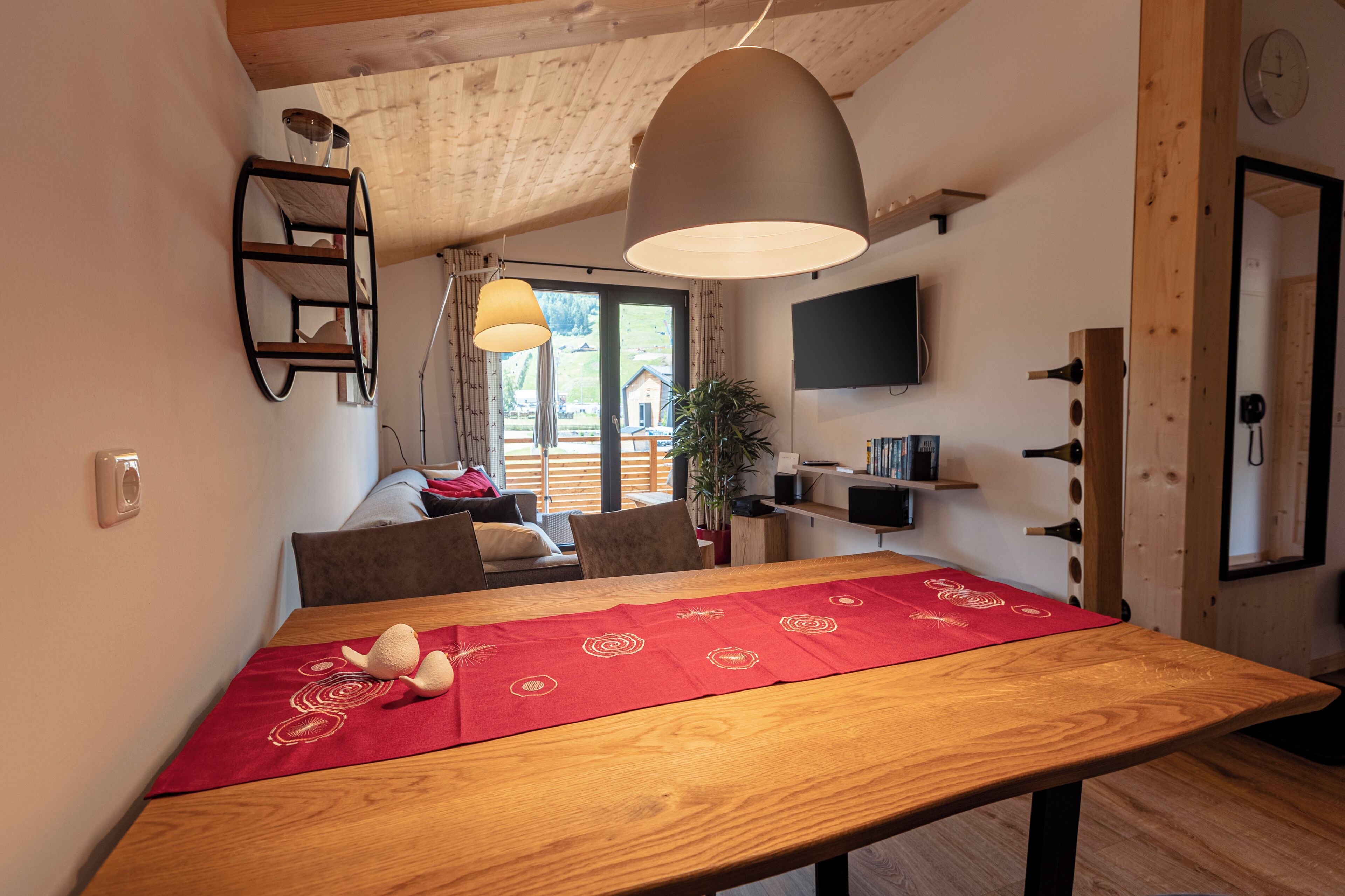 A dining area with a wooden table, red table runner, and a hanging pendant light.