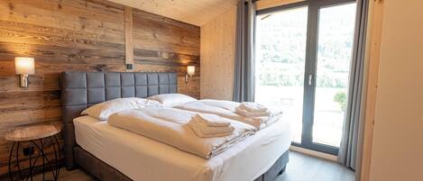 A bedroom with a wooden headboard, a large bed with white linens, a round side table, and a view of the outdoors through a sliding door.