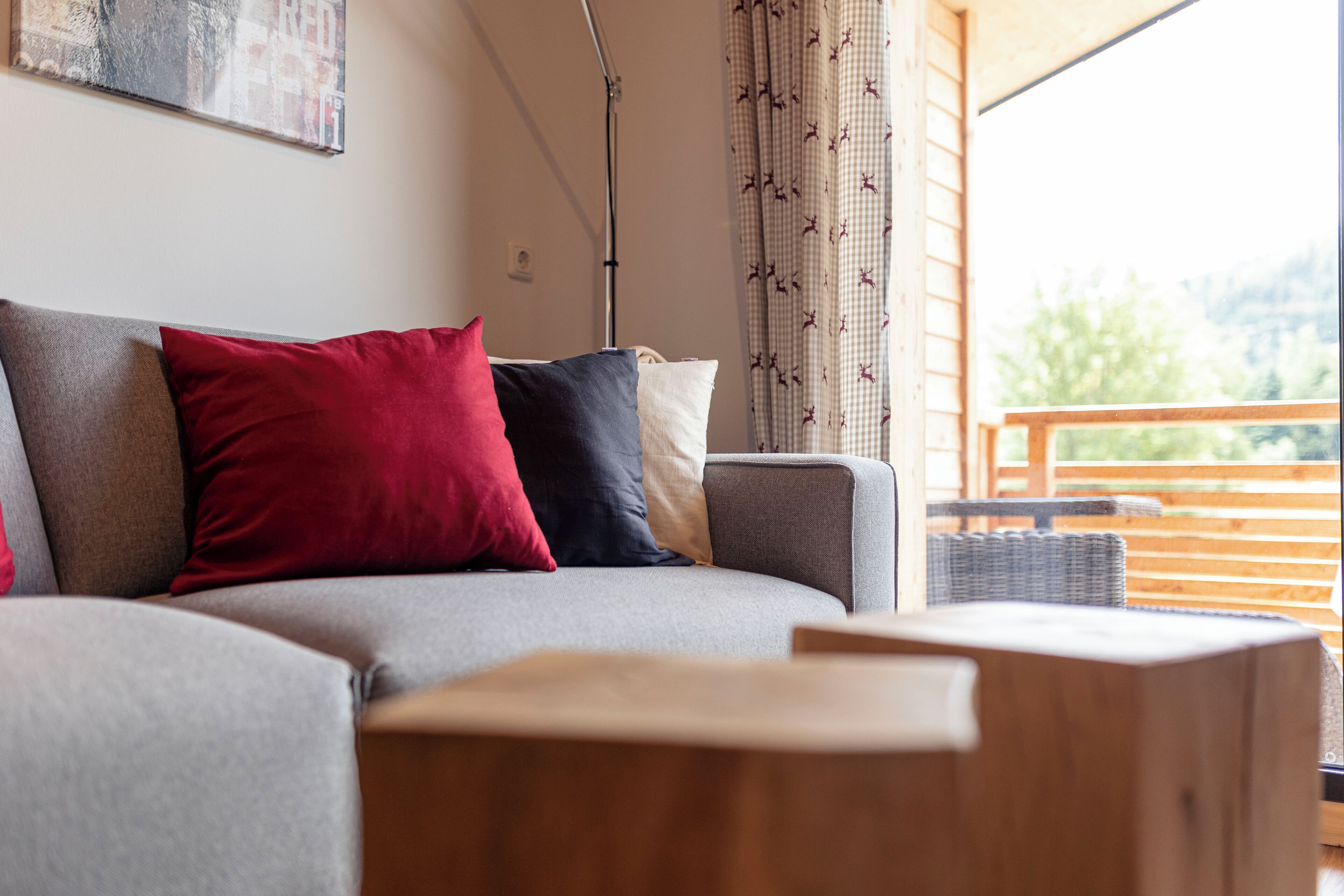 Ein modernes Wohnzimmer mit einem grauen Sofa, roten und blauen Kissen sowie einem Holztisch.
