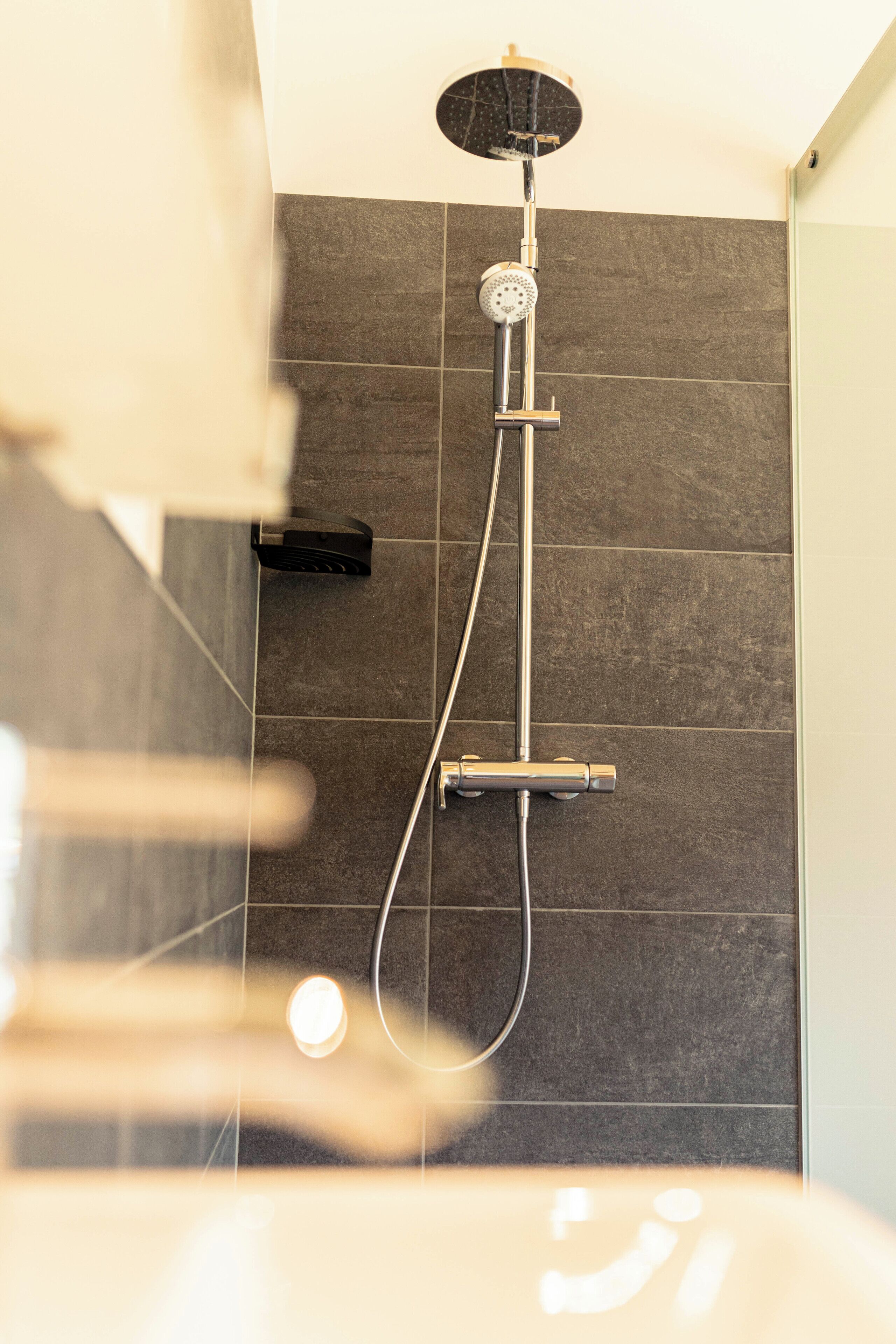 A shower with a handheld showerhead and a wall-mounted control panel.