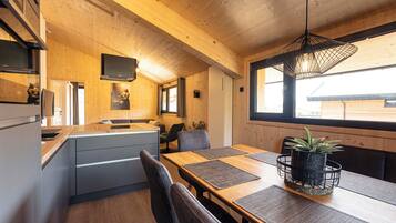 A modern kitchen with wooden walls, a built-in fridge, and a dining area with a wooden table and chairs.