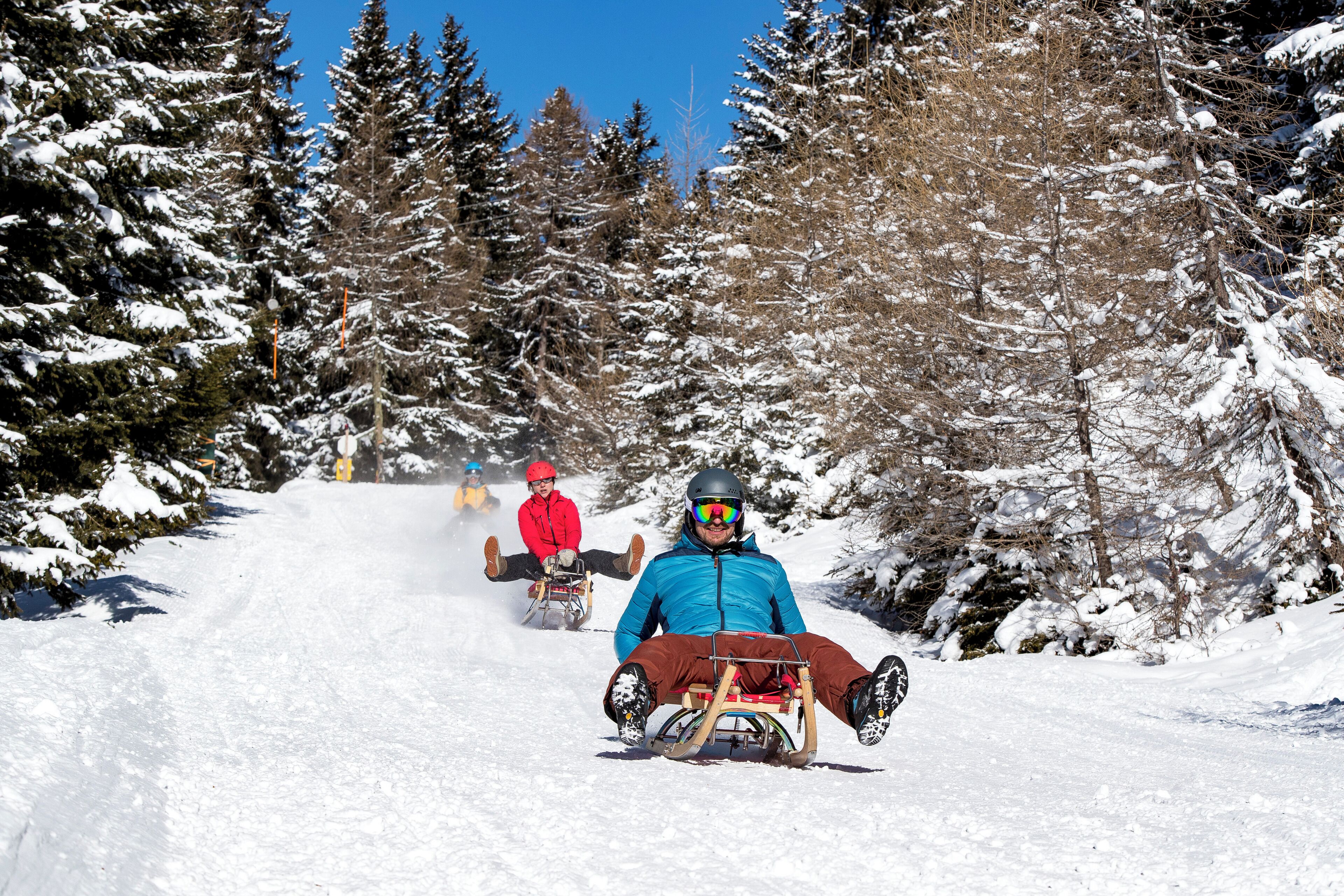 A snowy ski slope with a person in a blue jacket and helmet sitting on a sled.