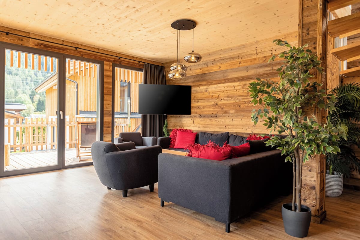 A modern living room with a sofa, armchairs, a flat-screen TV, and a potted plant.