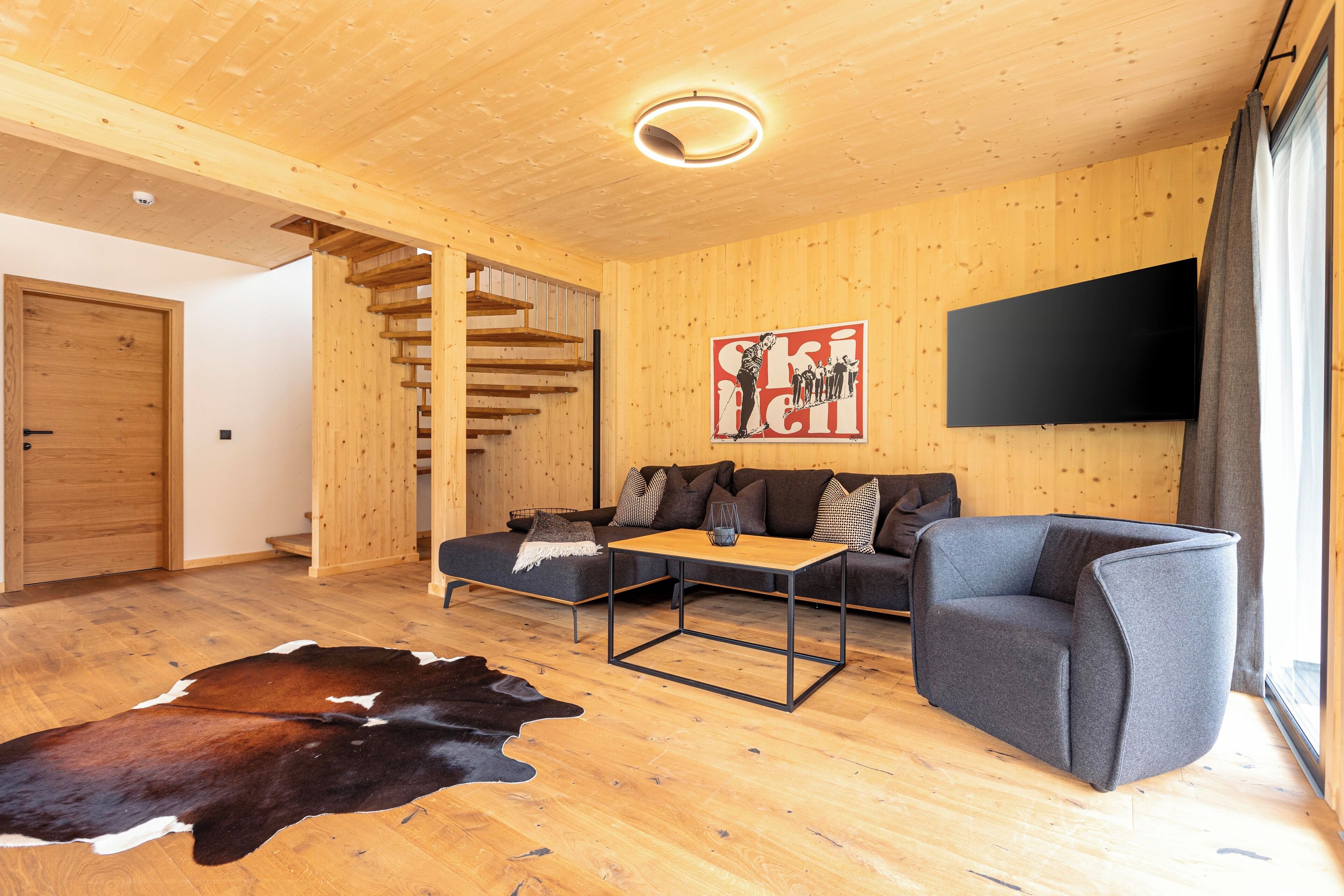 A modern living room with wooden floors, a sofa, a coffee table, and a mounted TV.