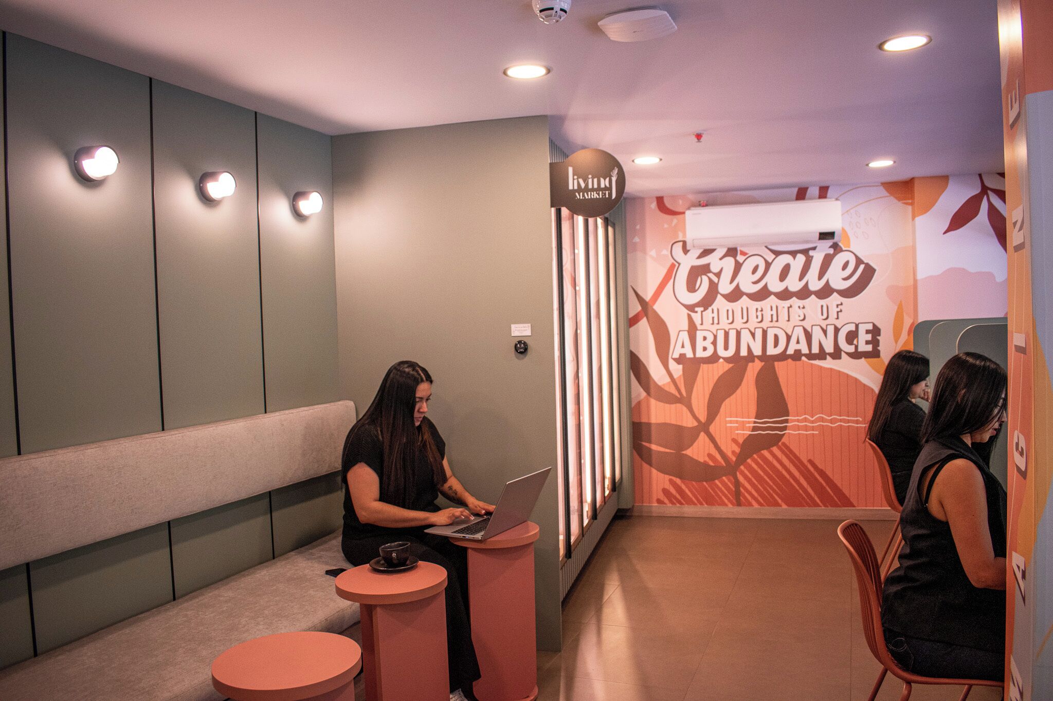 A modern interior with a seating area, a person using a laptop, and a wall with motivational text.