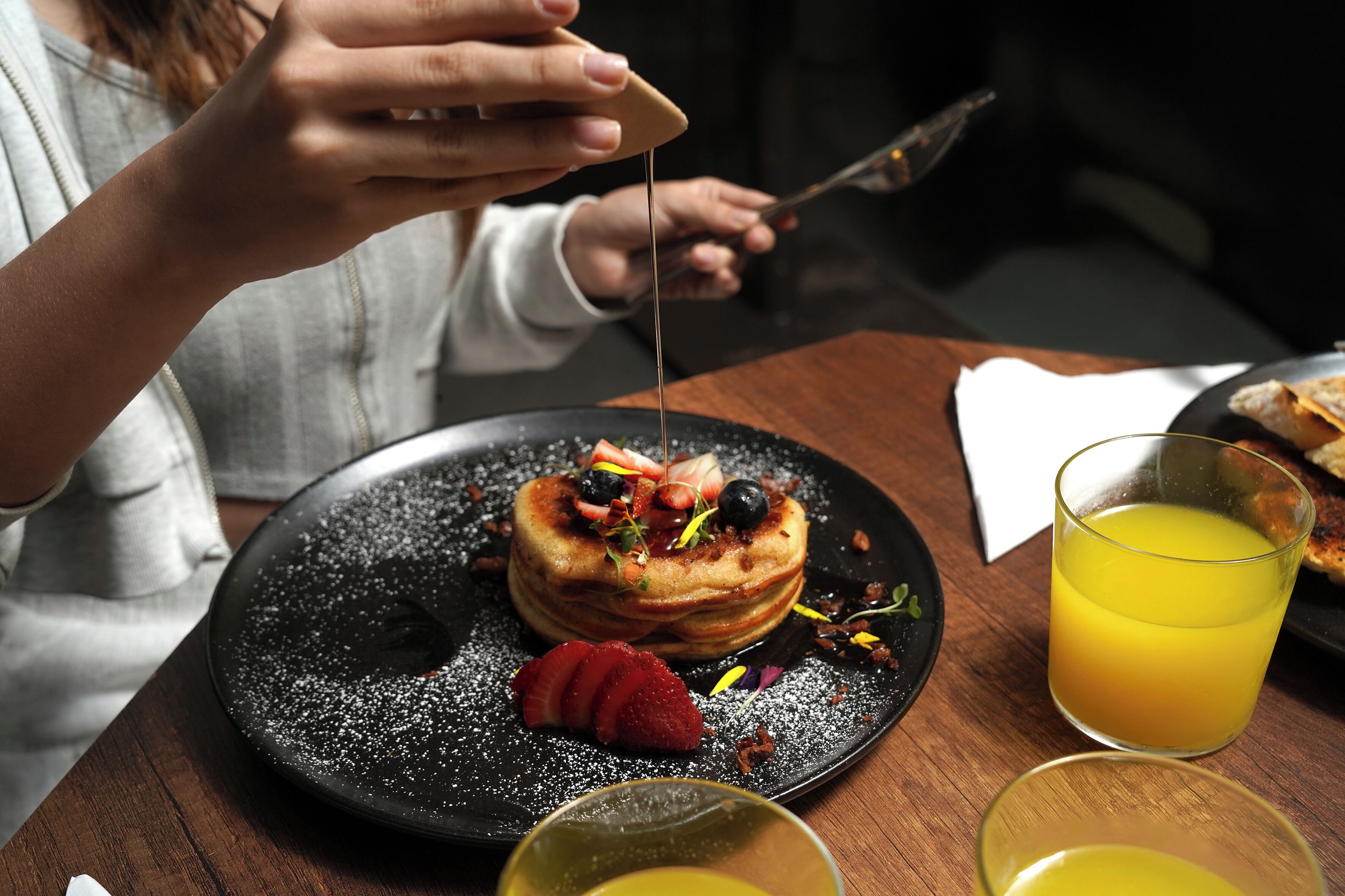Un desayuno con tortitas, fresas y un vaso de zumo de naranja sobre una mesa de madera.
