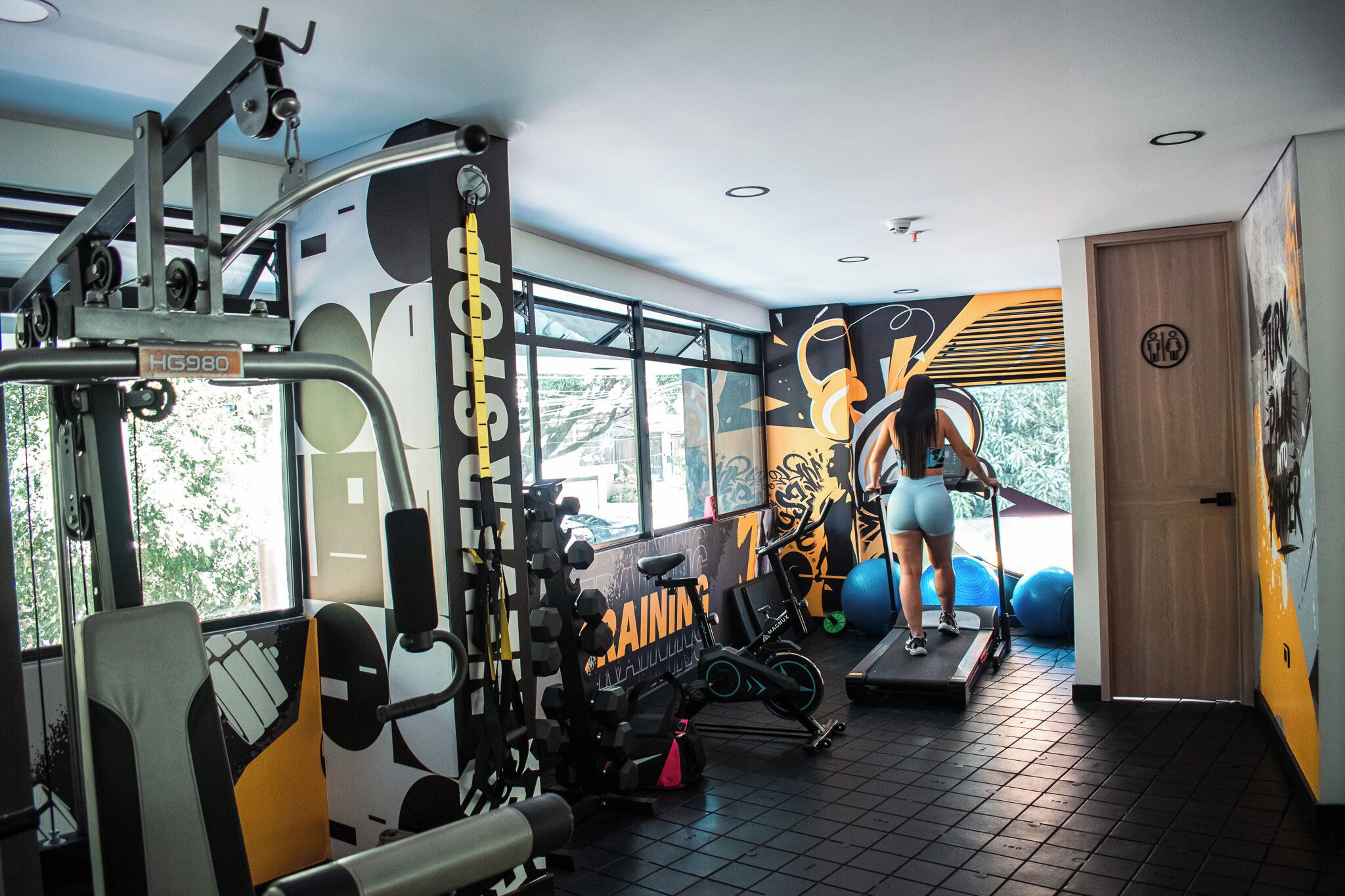 Ein Fitnessstudio mit Trainingsgeräten, Laufband und einem großen Fenster.