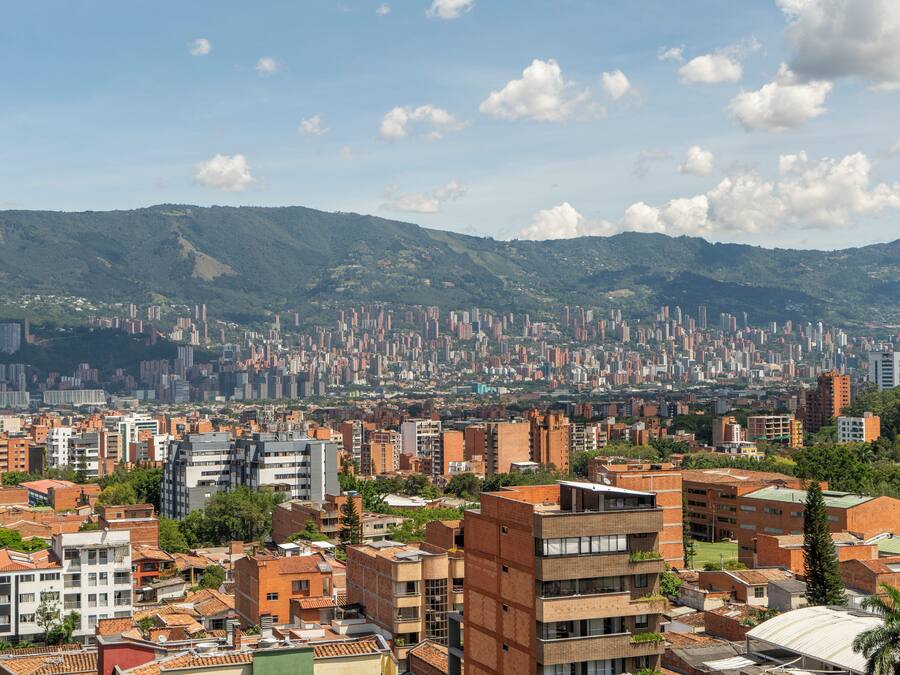 A cityscape with a mix of residential and commercial buildings, a prominent hill in the background, and a clear sky.