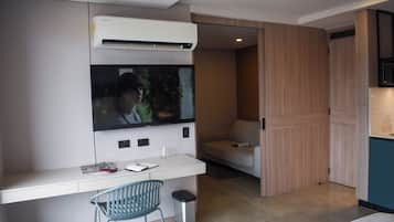 A modern room with a white desk, a mounted TV, a small trash bin, and a blue chair.